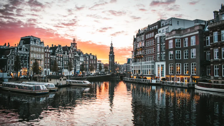 Canal de Ámsterdam al atardecer con casas tradicionales y botes
